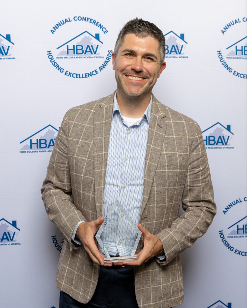 A smiling man in a plaid blazer holding a clear award trophy.