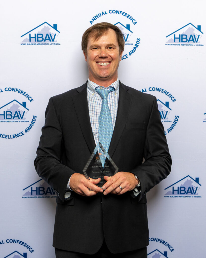A man in a suit and tie holding a glass award at the HBAV Annual Conference & Housing Excellence Awards.